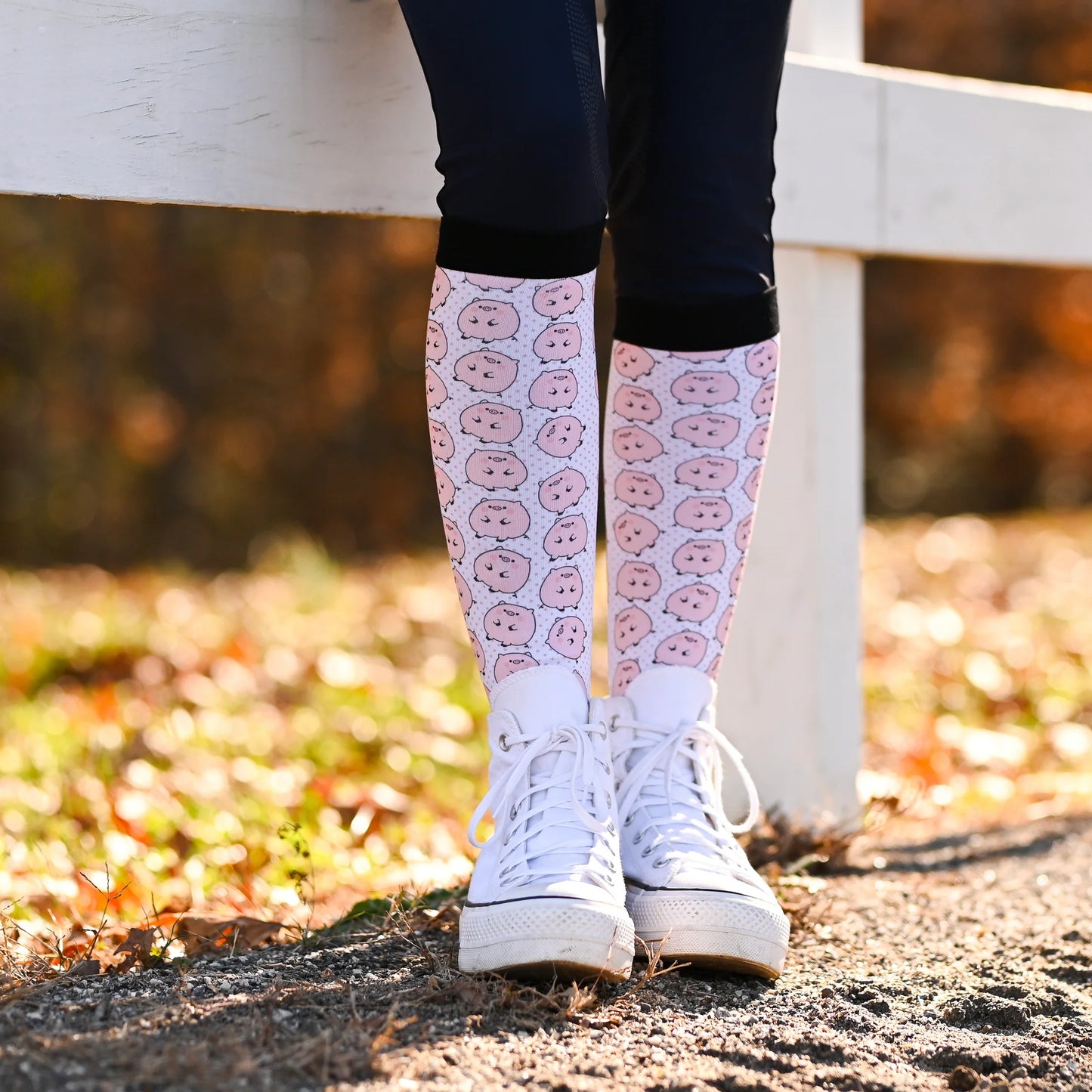 Person wearing pink knee-high socks with a piggie pattern and white sneakers outdoors.