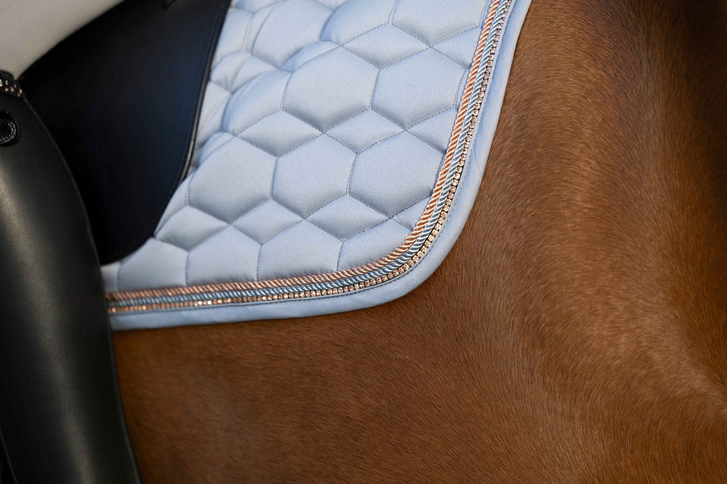 showing the corner of a saddle pad on a bay colored horse. Grey pad with rosegold trim