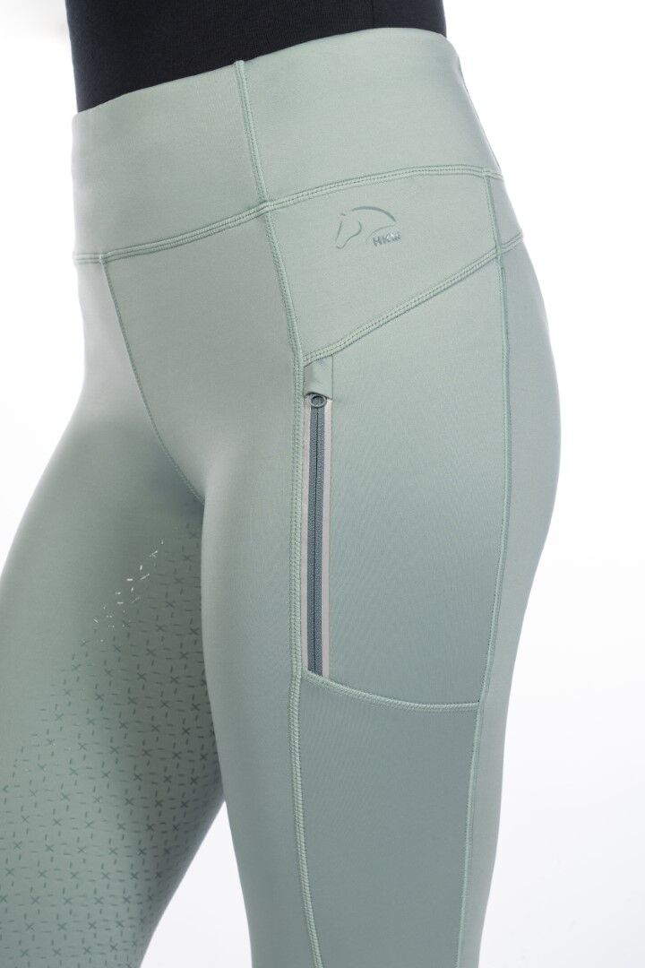Side view of sage green equestrian riding tights with same colored embroidered HKM logo on hip