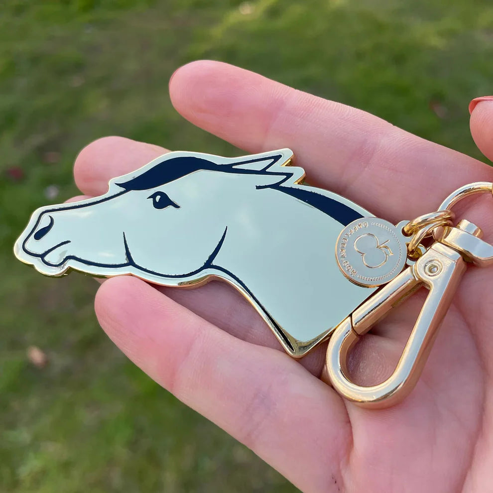 Keychain with horsehead - ears flat -design held in a hand against a grassy background