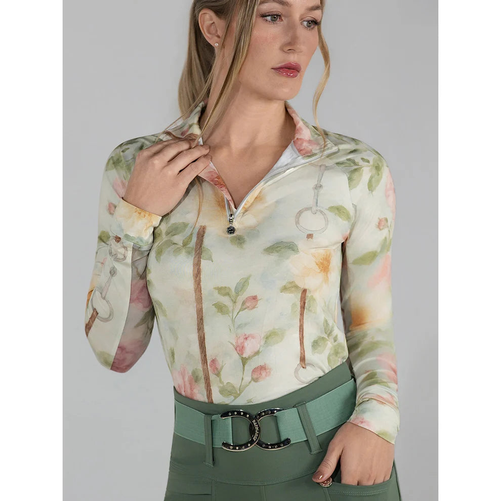 Woman wearing a floral 1/4 zip riding shirt with a green belt against a gray background