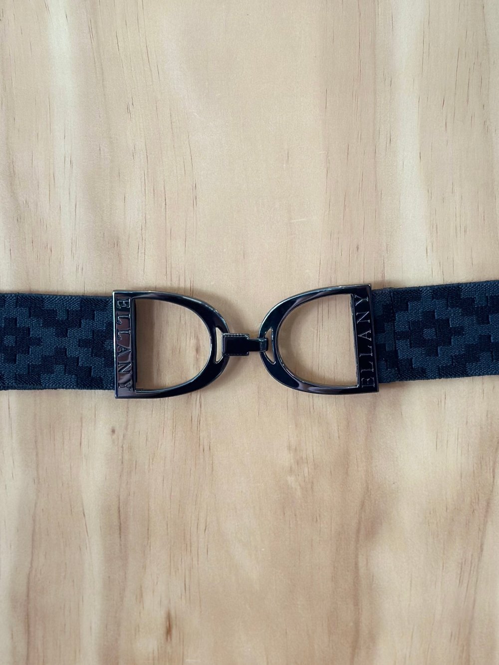 Black textured elastic belt with a dark buckle that looks like a pair of equestrian stirrups
