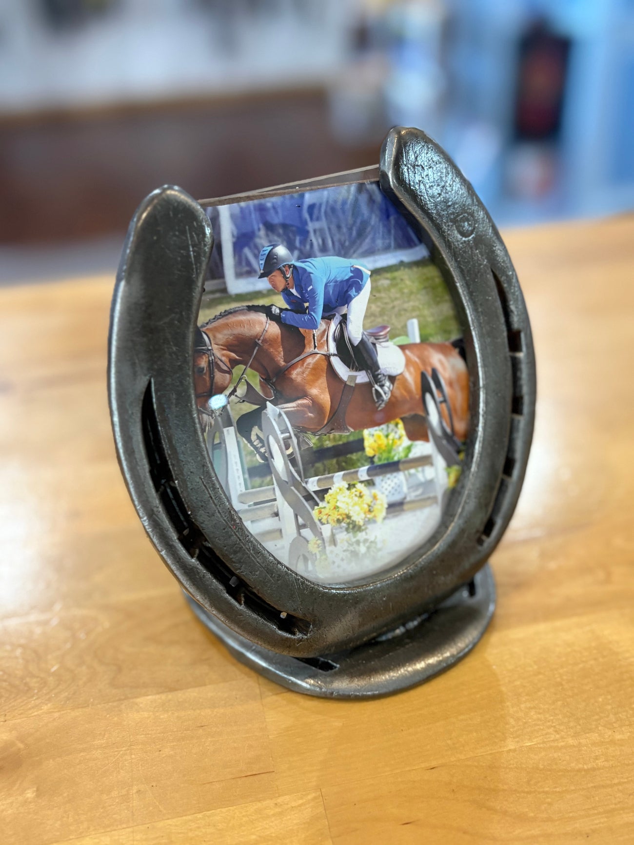 Horseshoe frame with a picture of a rider jumping a horse inside, placed on a wooden surface.