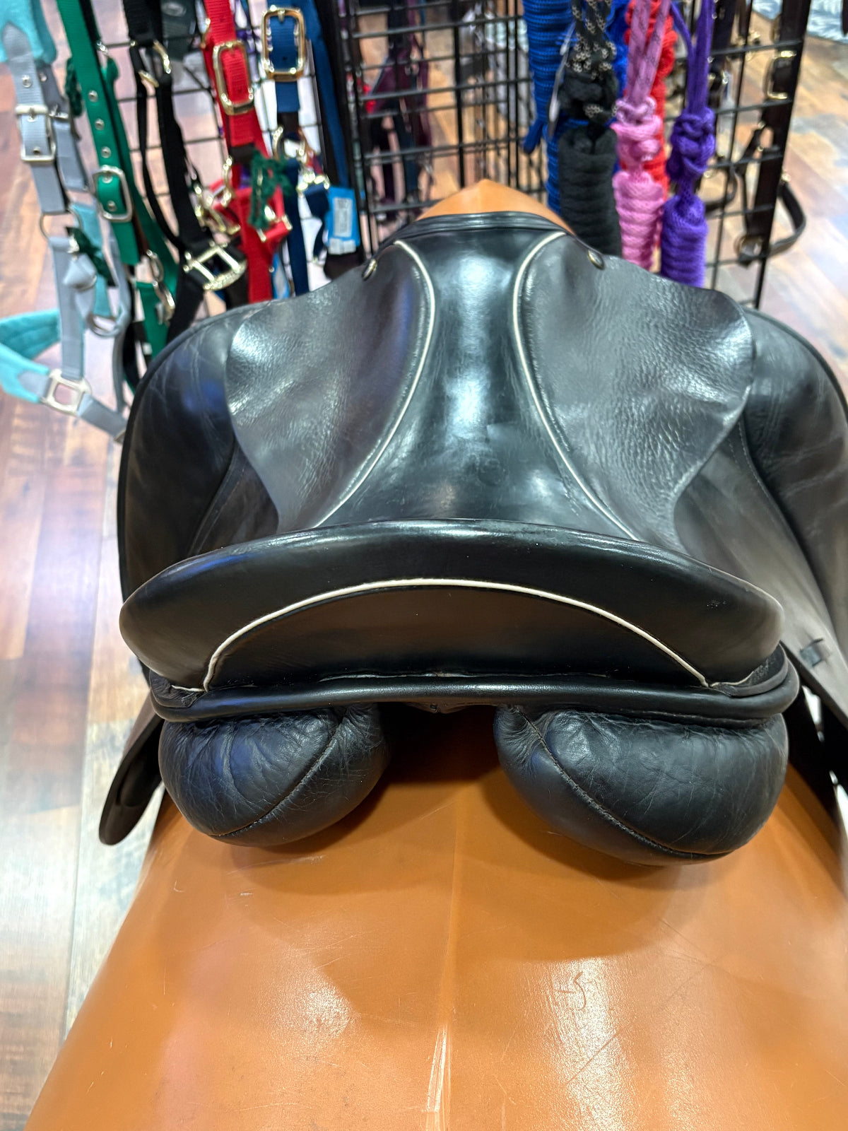 A black leather horse saddle photographed from above, resting on a tan display stand inside a store.