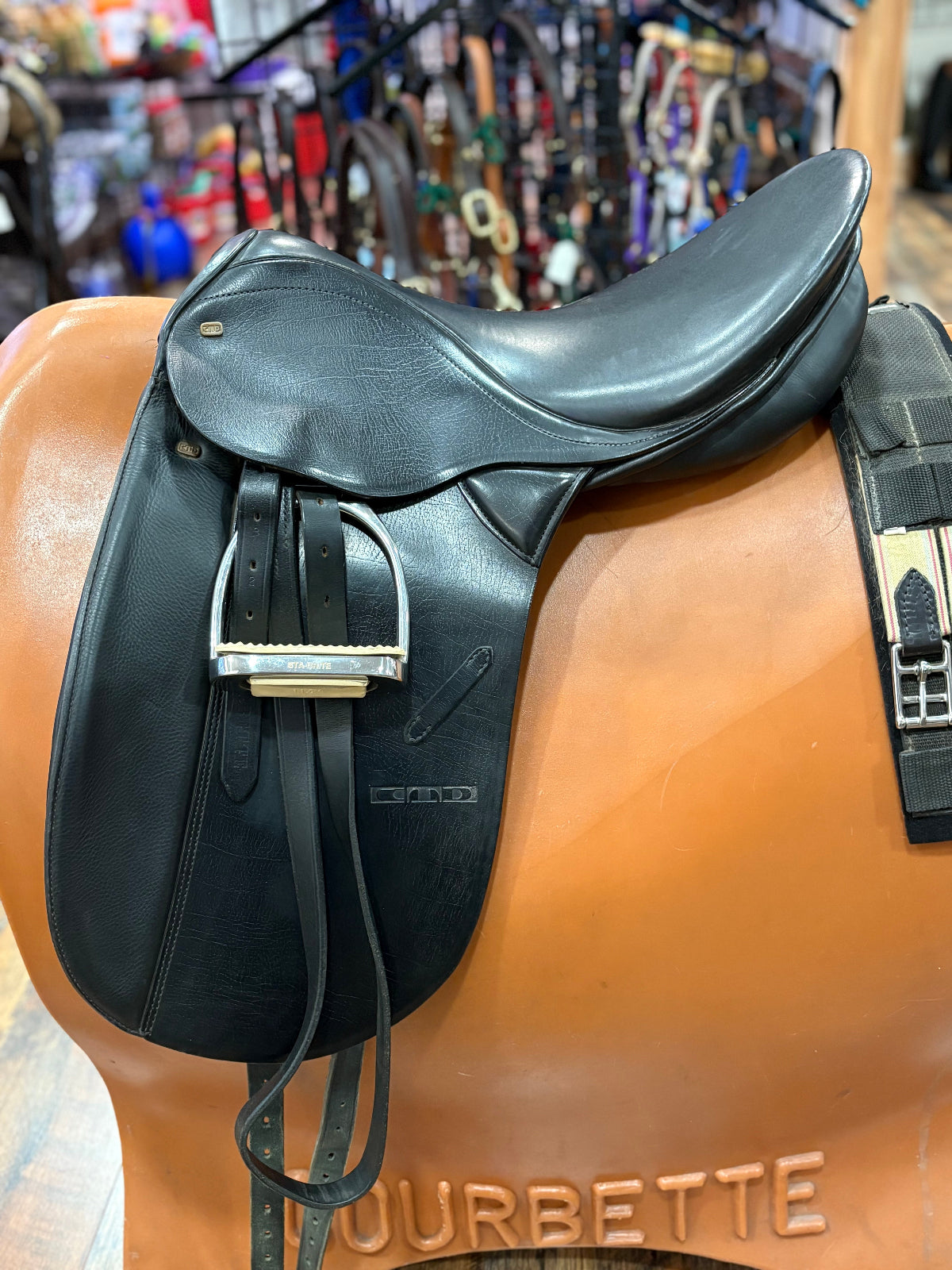 Black dressage saddle shown with rolled up stirrup and girth