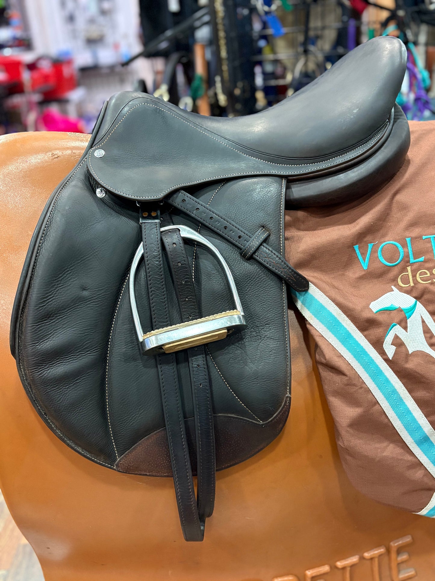 Dark leather english saddle with stirrups. Shown on top of a Voltaire saddle cover.
