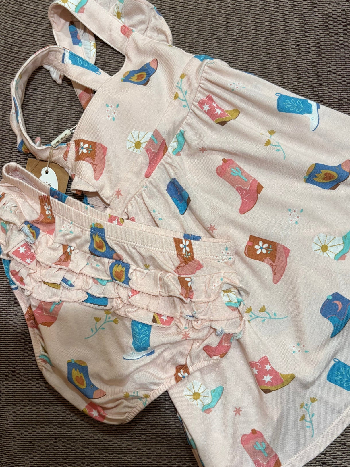 Baby romper with cowboy boot pattern on a textured surface