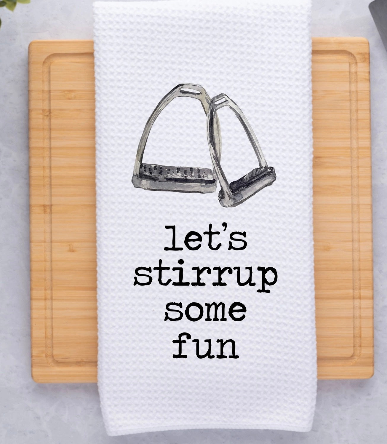 White waffle dish towel with a picture of a pair of equestrian stirrups and the saying, "let's stirrup some fun"