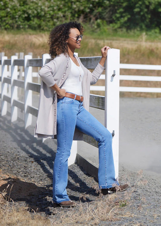 Woman standing near a fence modeling a beige cardigan sweater with equestrian Dee Bit design down the front.  below hip length