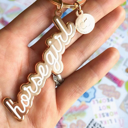 Hand holding a rose gold key chain that is a cursive word "horse girl"