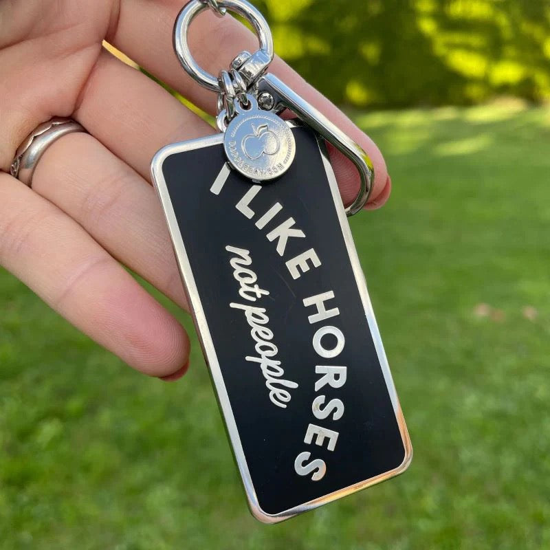 Handing holding a key chain that says I like horses not people