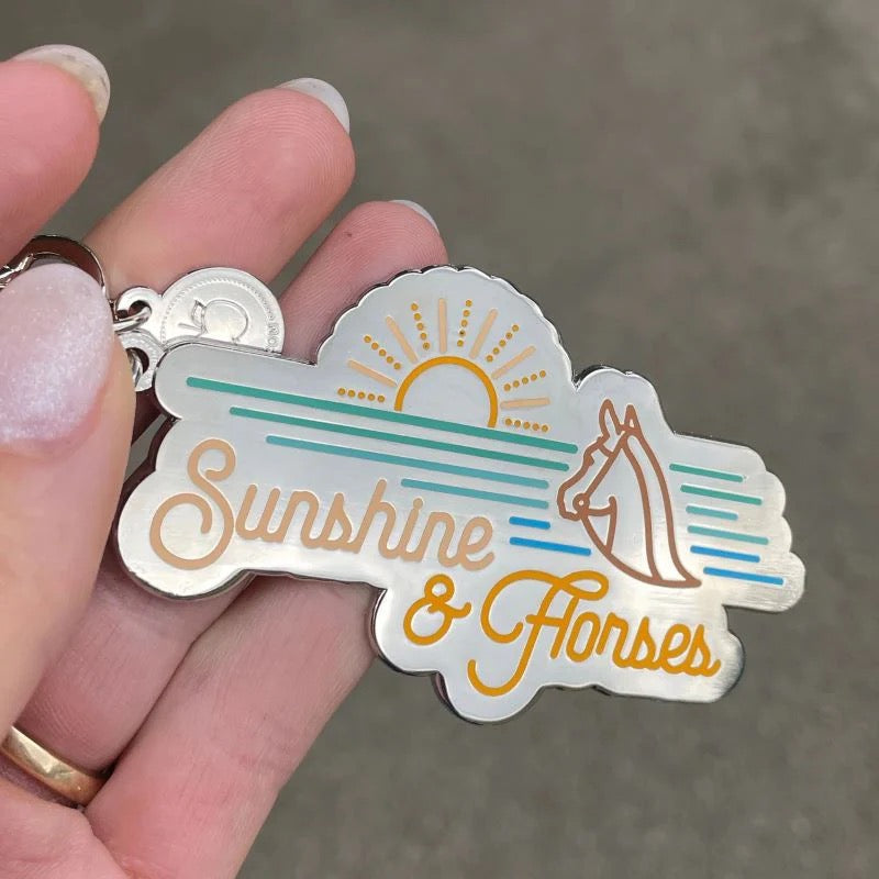 Hand holding a key chain that says Sunshine & Horses
