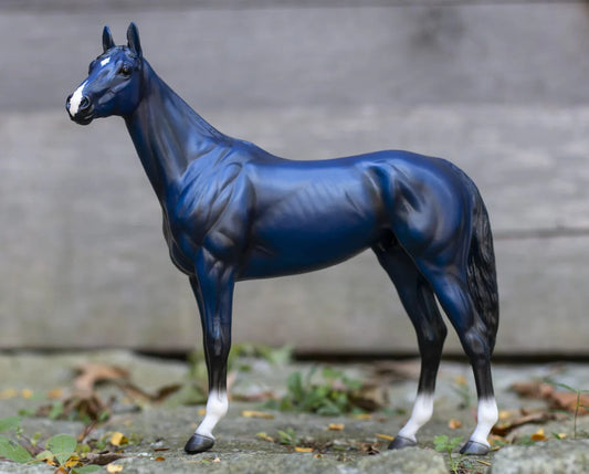 Blue /black horse with white socks figurine standing on a concrete surface with a blurred background