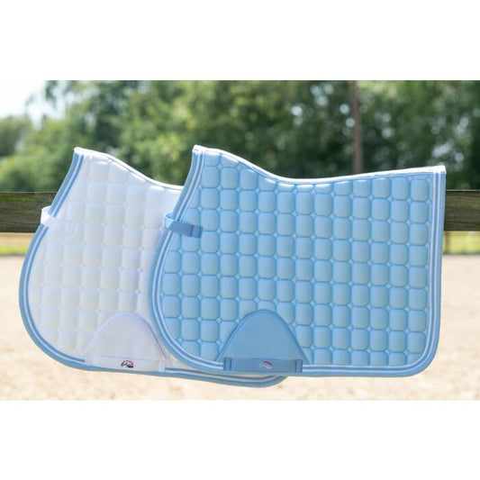 two equestrian saddle pads one white with blue piping laying 3/4ths underneath blue saddle pad with white piping, both sitting on a wooded fence beam with blurred trees in the background  