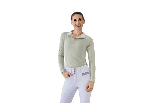 Woman wearing a light green long-sleeve top and white pants on a white background
