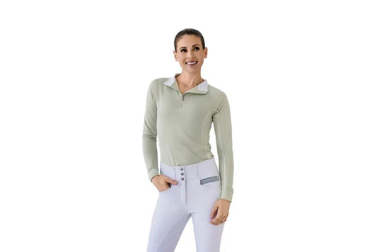 Woman wearing a light green long-sleeve top and white pants on a white background