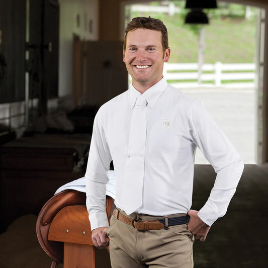 Man in a white shirt standing next to a horse saddle in an indoor setting