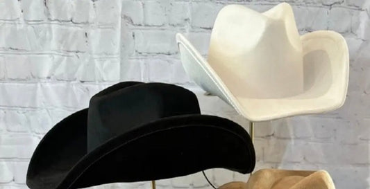 front view of both black and ivory suede equestrian cowboy hats with a white brick wall background