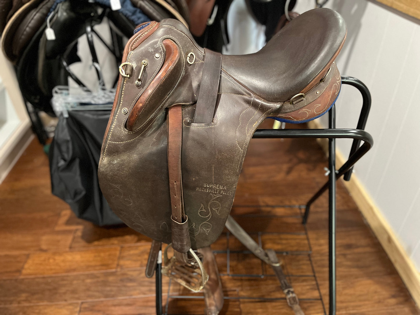 dark brown with lighter brown leather accents on a Australian stock saddle sitting on a black saddle holder. view on the left side
