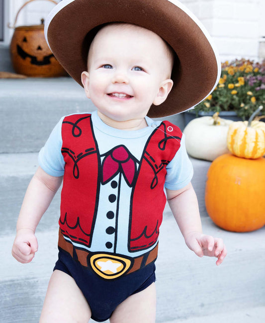 Baby wearing a cowboy-themed onesie with pumpkins and a hat in the background