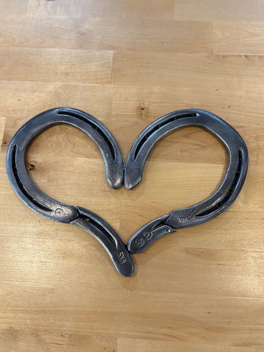 Two horseshoes shaped like a heart on a wooden surface