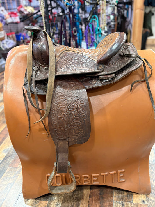 Brown leather saddle with intricate designs on a mannequin in a store setting.