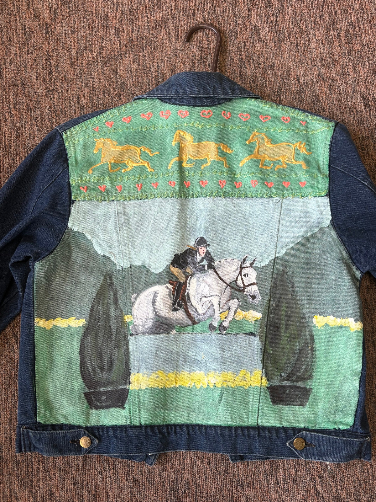 Back of a denim jacket with a painted horse and rider design.