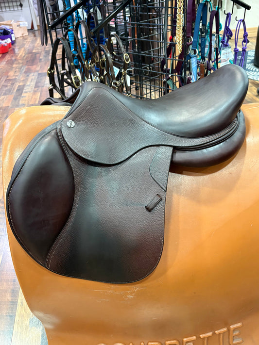 Brown leather english saddle on a stand with a blurred background.