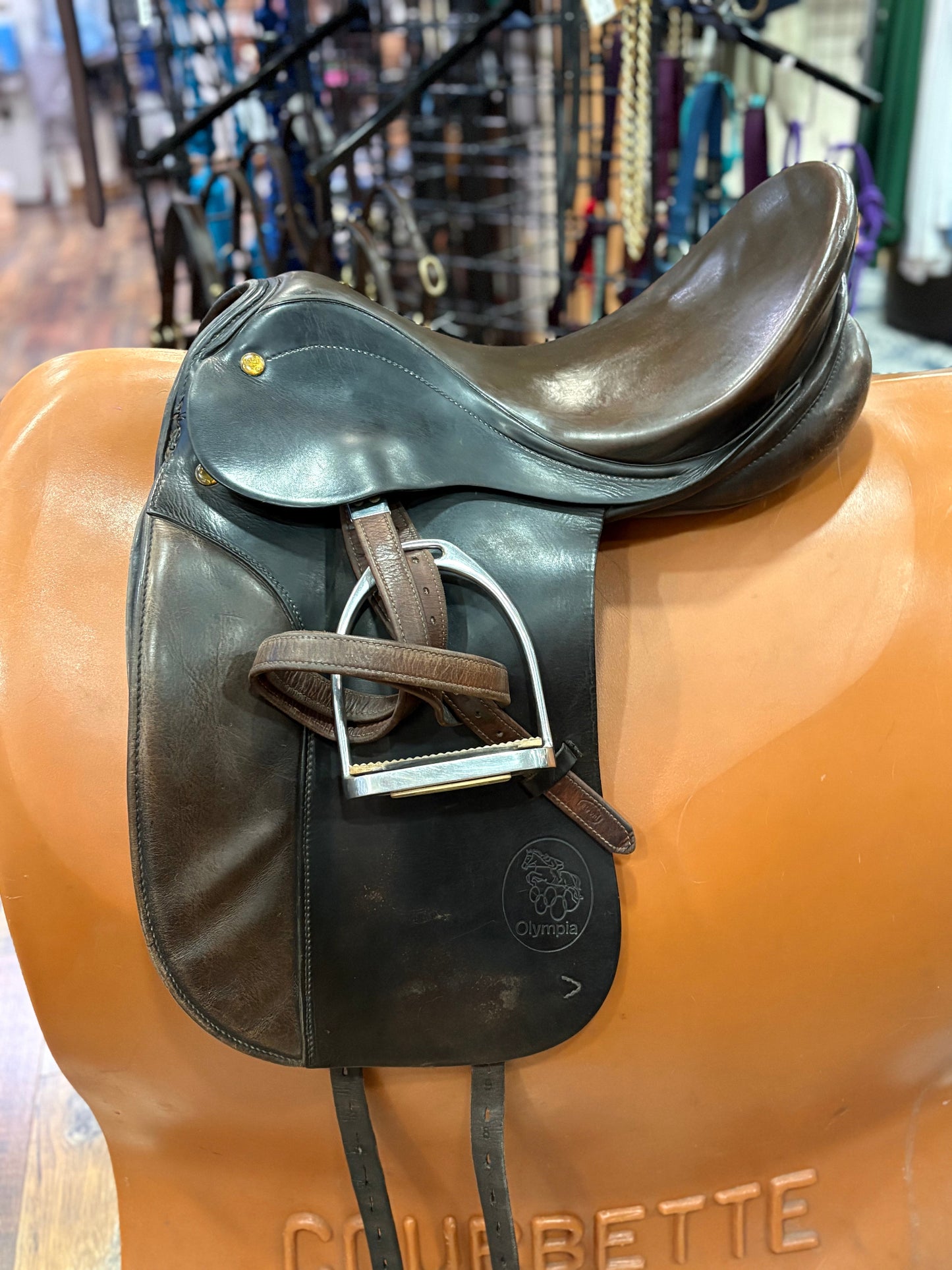 Black and brown leather dressage saddle shown on a stand with stirrup leathers and irons.