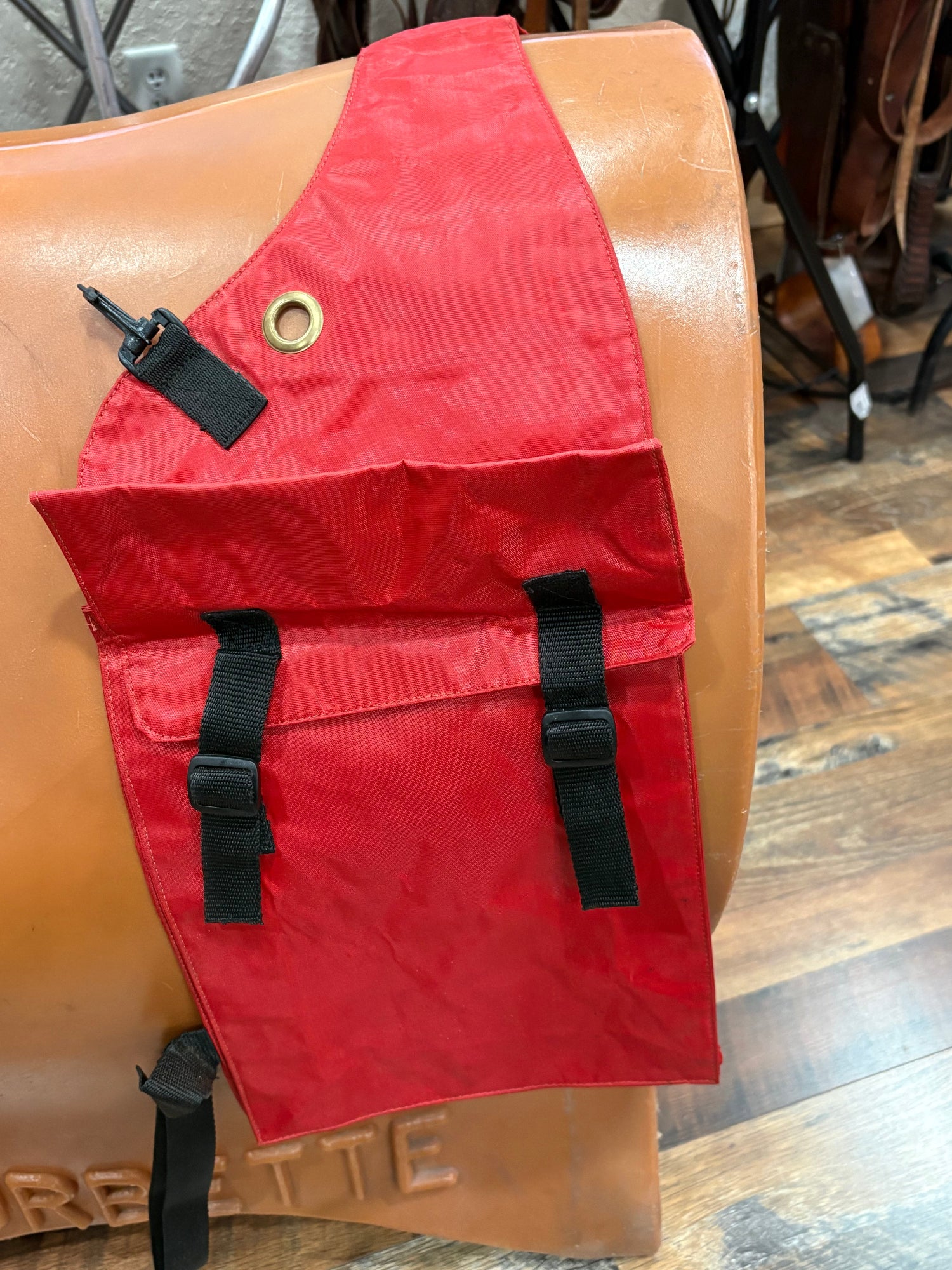 A red waterproof saddle bag with black straps and a brass grommet, shown draped over a saddle stand