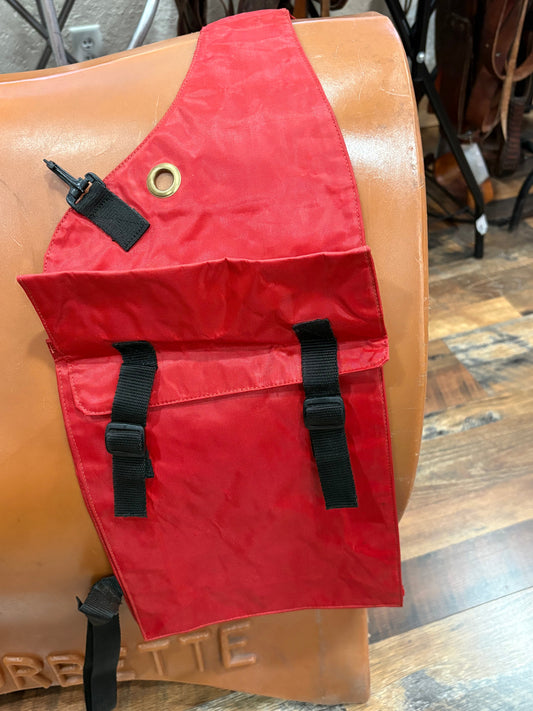 A red waterproof saddle bag with black straps and a brass grommet, shown draped over a saddle stand