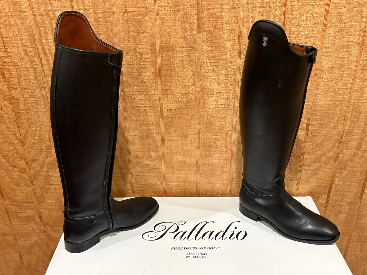 A pair of black leather tall riding boots displayed on a white box with the brand name 'Palladio' printed on it, set against a wooden background.