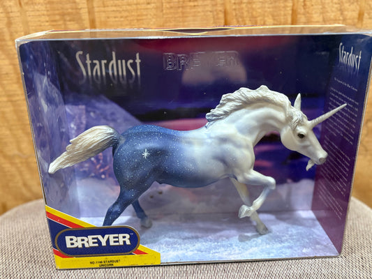 Breyer Stardust unicorn toy model in its original retail packaging, displayed on a textured fabric surface with a wooden background.