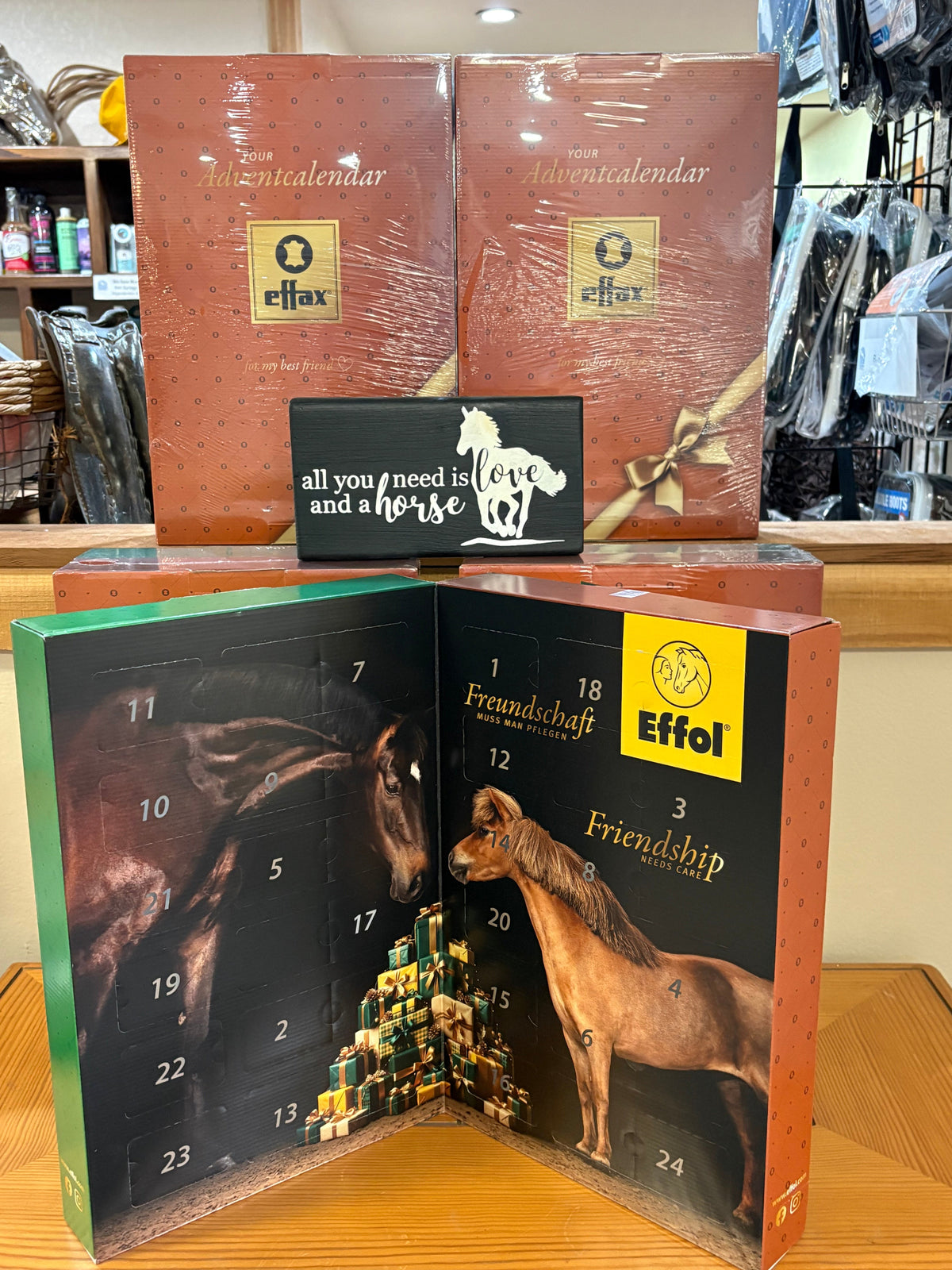Boxed advent calendars displayed on a wooden table in a retail setting. The closed boxes are wrapped in clear plastic and labeled Effol, while the open calendar in front shows illustrated horse artwork, numbered advent panels.