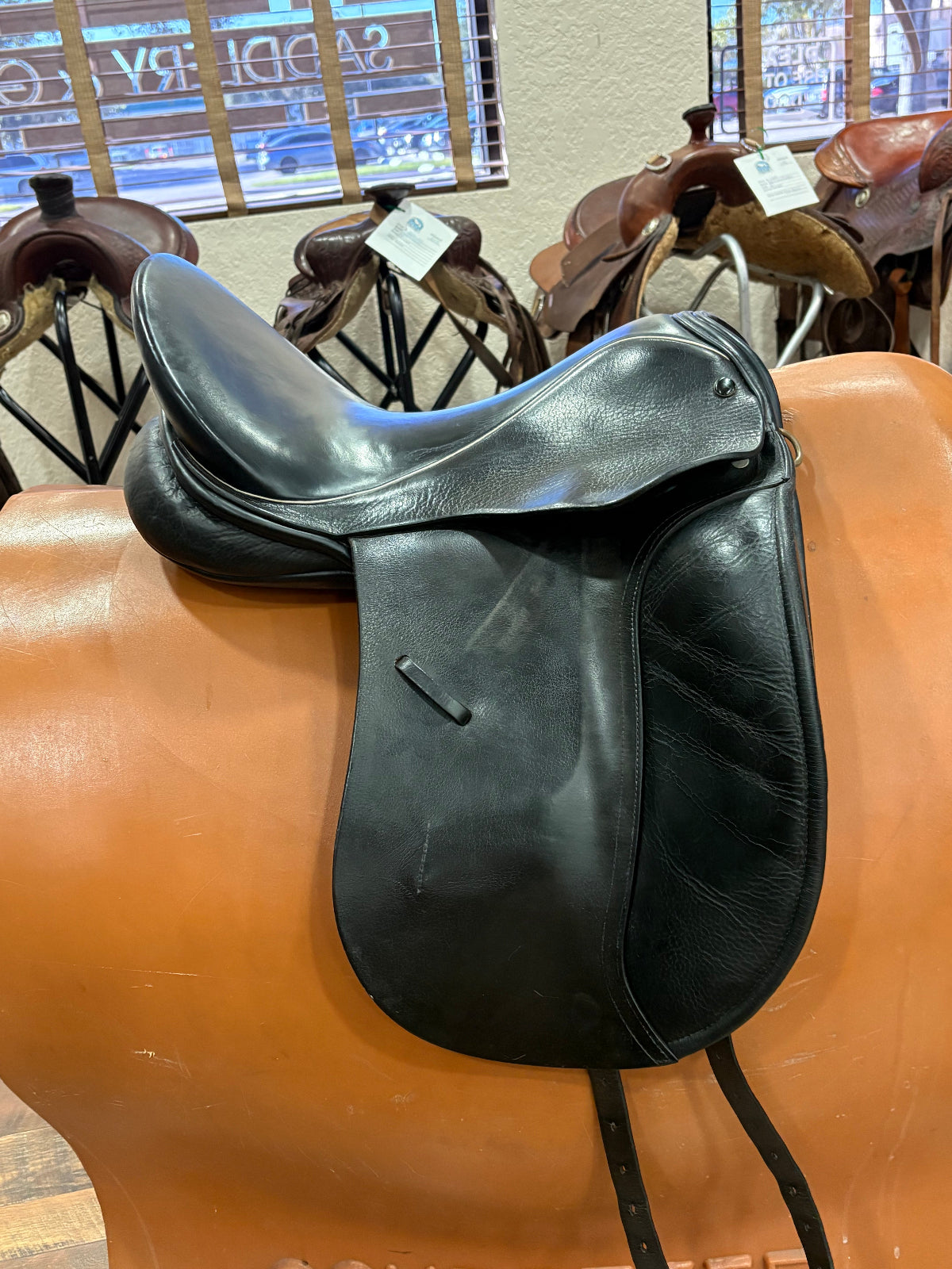 Side view of a black leather dressage saddle on a stand taken in a retail environment.