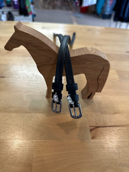 black leather equestrian spur straps with silver buckles with silver two peas in a pod charm resting on wooden horse model