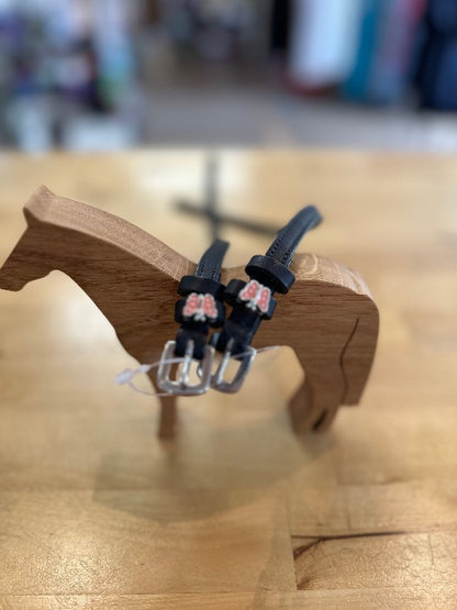 black leather equestrian spur straps with silver buckles with pink and sliver butterfly charm, resting on wooden horse model