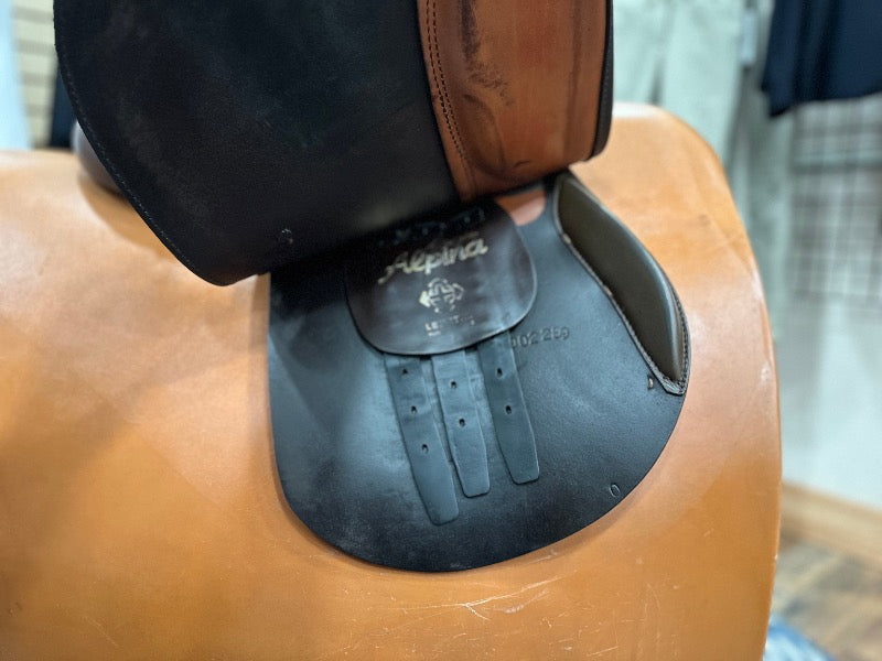 The flap of a brown leather english saddle is lifted showing billet straps in perfect condition