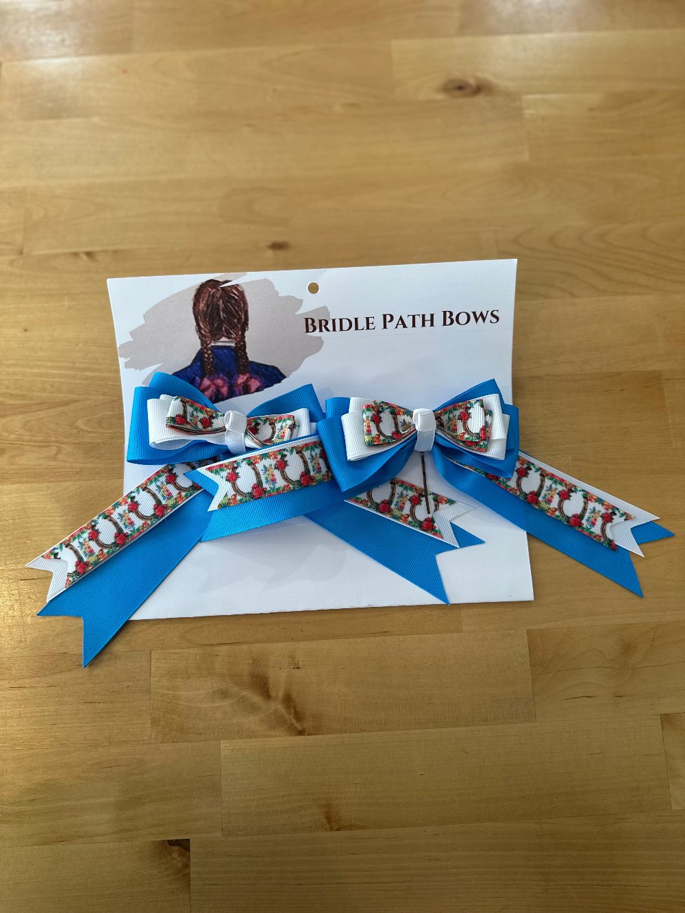 Image of children’s horse riding show bows, white and blue with stirrup and flower pattern