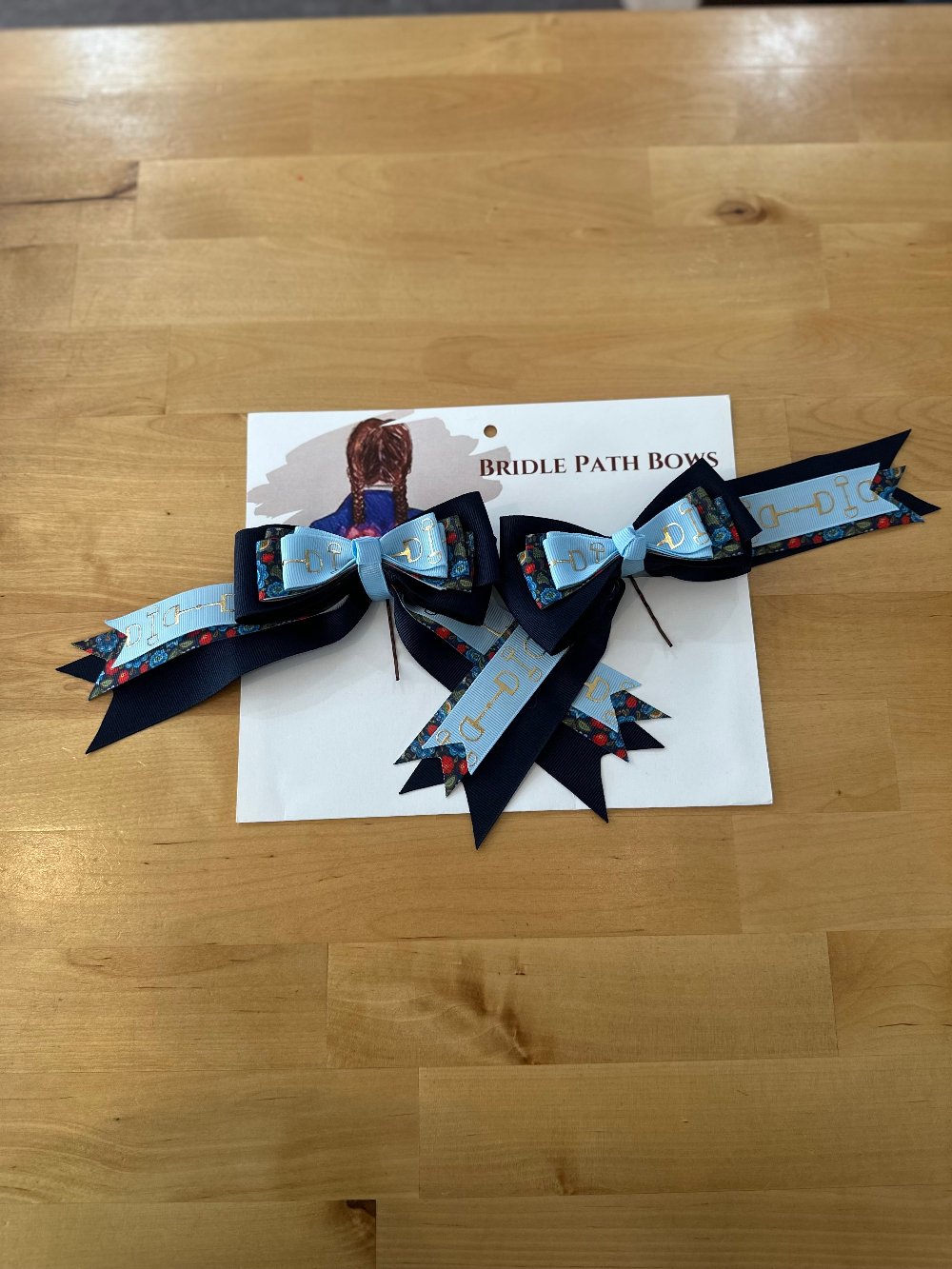 Image of children’s horse riding show bows, dark and light blue with silver stirrup pattern and flowers