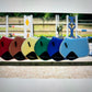 multiple saddle pads of different colors hung on a fence railing.  