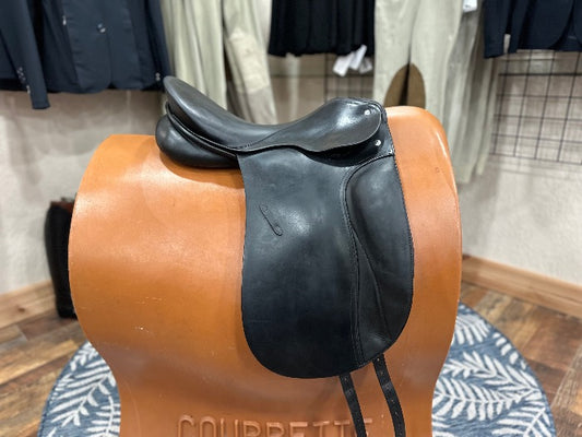 right view of black equestrian leather dressage saddle on brown saddle model with tan show equestrian pants and black show coats in the background