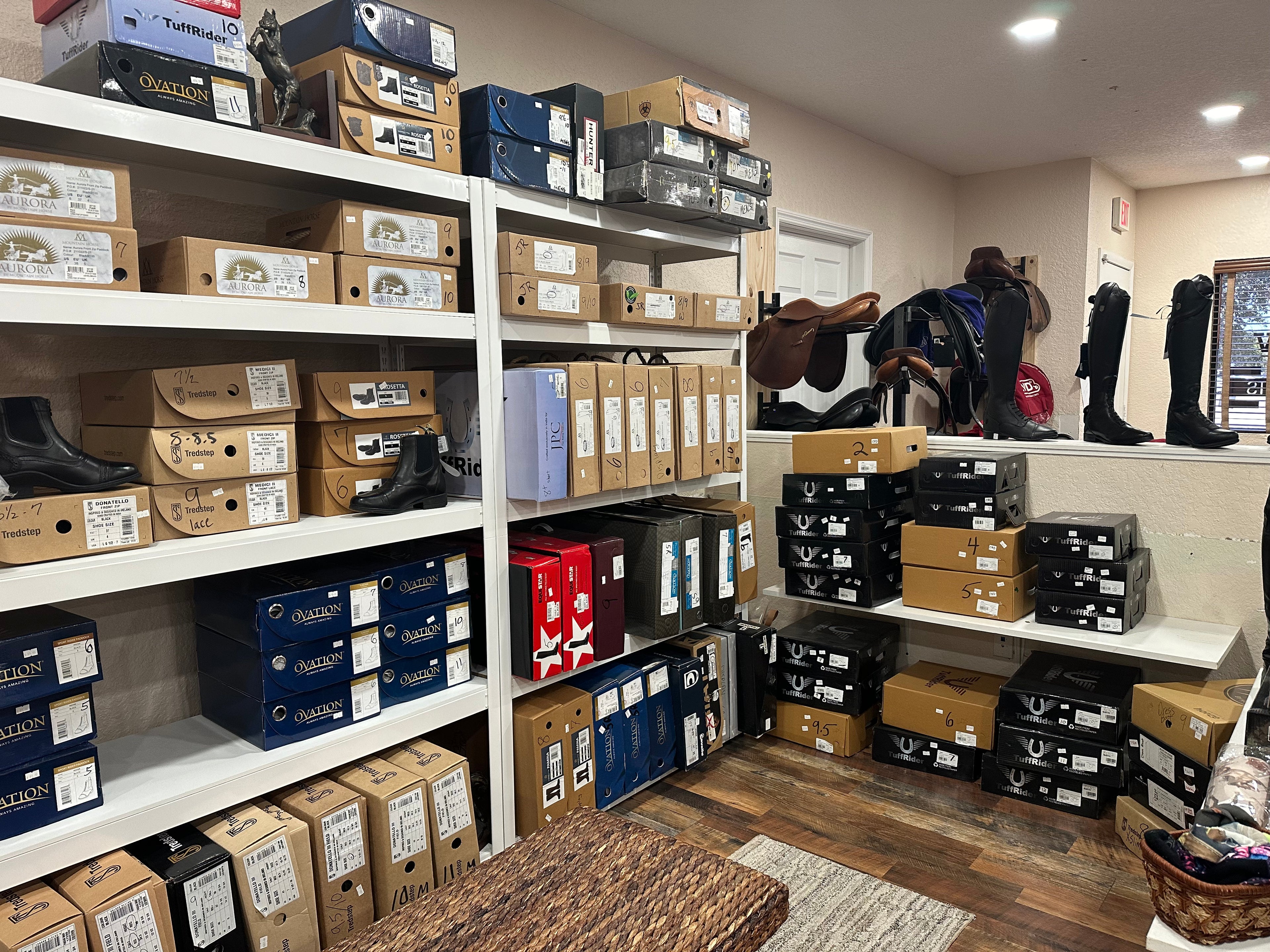 overview of store, boot section on the left paddock boots, then in the middle are tall boots, right side is western boots with model tall boots above. in the far back top right are some consignment saddles 