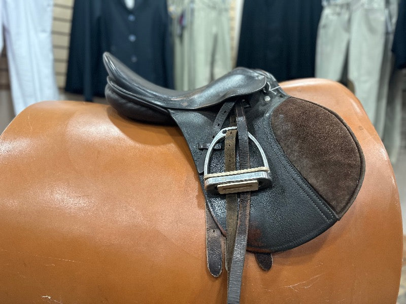 Side view of a dark brown leather english saddle with silver stirrup irons and suede patch knee rolls.