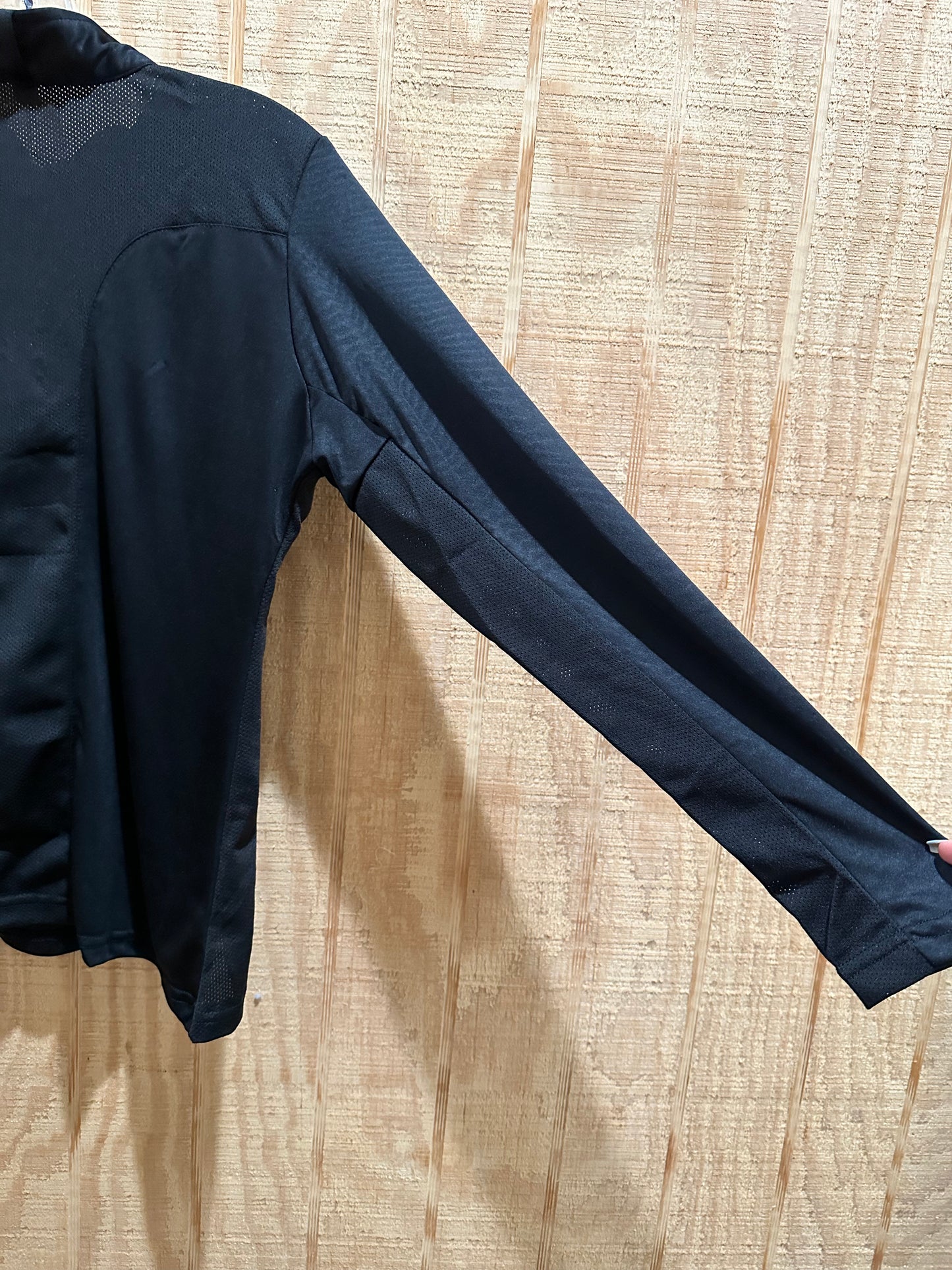 right sleeve of a black long sleeve riding shirt hung up against light colored wood