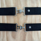 Two black elastic belts displayed against a woodgrain background.  Each belt has a slightly different pattern.  Both have silver clasps and small silver logo.