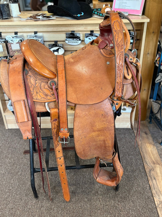 Light brown leather western saddle with fancy leather tooling.  shown with leather cinch, stirrups and breastplate.