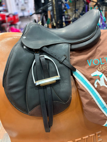 Dark leather english saddle with stirrups.  Shown on top of a Voltaire saddle cover.