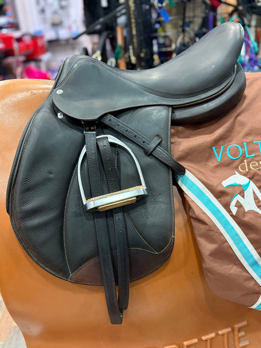 Dark leather english saddle with stirrups.  Shown on top of a Voltaire saddle cover.