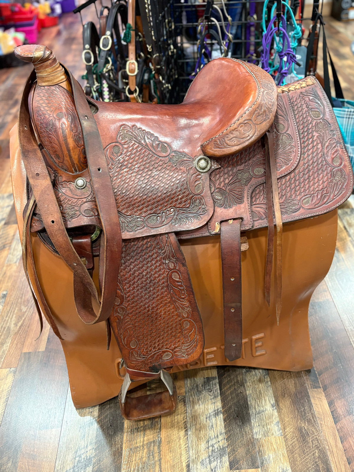 Brown leather western saddle shown on a stand.